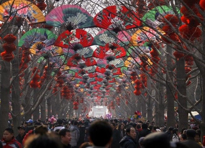 Толпы людей ходят среди деревьев украшенных красными фонарями на храмовой ярмарке в честь празднования китайского Нового года в Пекине