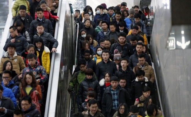 Люди спускаются на эскалаторе и сходят по лестнице направляясь к платформе метро в час пик в Пекине